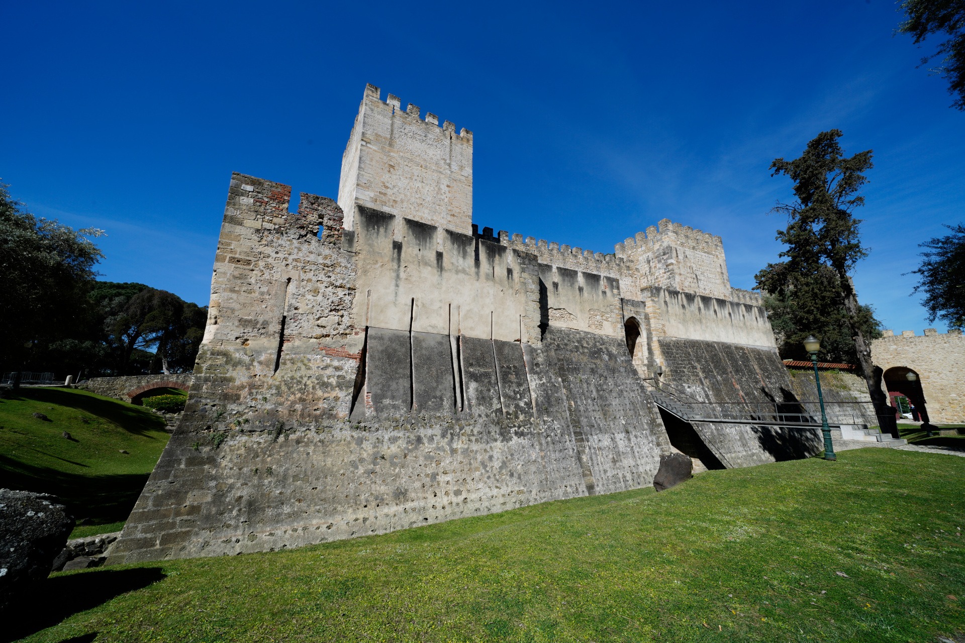 Descrição da imagem: fotografia da fachada do Castelo em que vemos a Torre de Menagem à esquerda, a entrada principal ao meio, e a Torre da Cisterna à direita.
